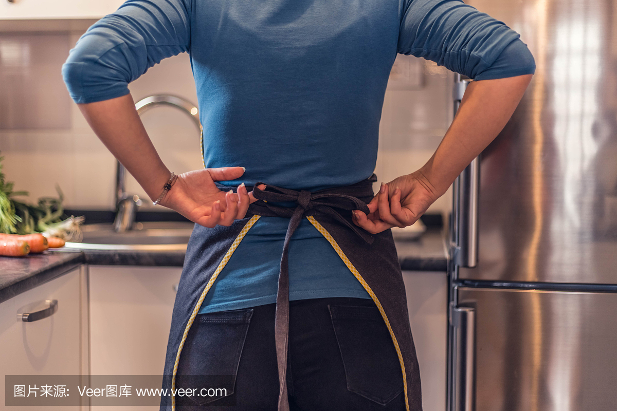 緊縮的圍裙。廚房里穿著圍裙的漂亮女人。